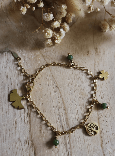 Bracelet Sissi en acier inoxydable doré orné de perles de jade verte et de charms symboliques — ginkgo, trèfle et arbre de vie — bijou porte-bonheur présenté sur fond naturel.