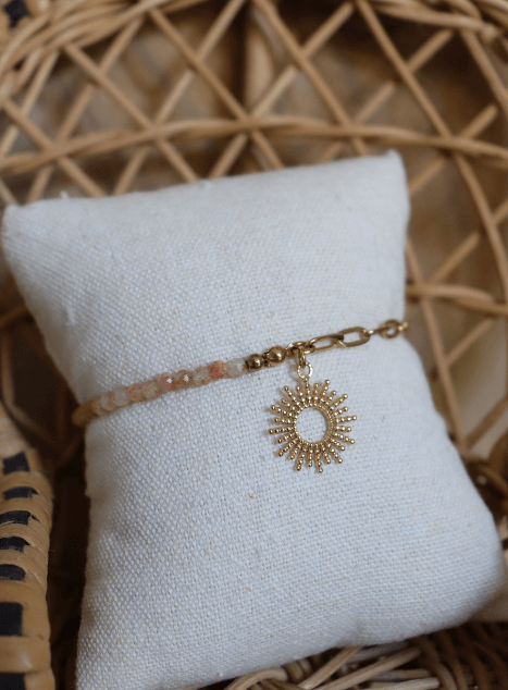 bracelet-chacha-pierre-de-soleil-pendentif-soleil-acier-inoxydable-dore.jpg Bracelet Chacha en acier inoxydable doré avec perles de pierre de soleil et pendentif soleil, bijou lumineux présenté sur coussin en lin dans une chaise en rotin.