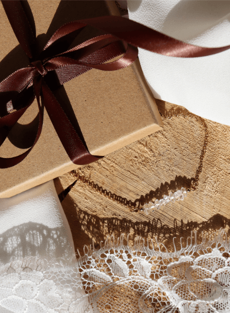 collier-lucia-diamant-herkimer-acier-inoxydable-dore-bijou-mariage.jpg Collier Lucia en acier inoxydable doré orné de perles de diamant d’Herkimer, bijou lumineux et raffiné présenté sur fond de dentelle et coffret cadeau.