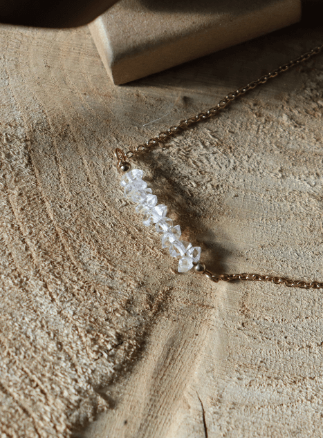 collier-lucia-diamant-herkimer-acier-inoxydable-dore-bijou-mariage.jpg Collier Lucia en acier inoxydable doré orné de perles de diamant d’Herkimer, bijou lumineux et raffiné présenté sur fond de dentelle et coffret cadeau.