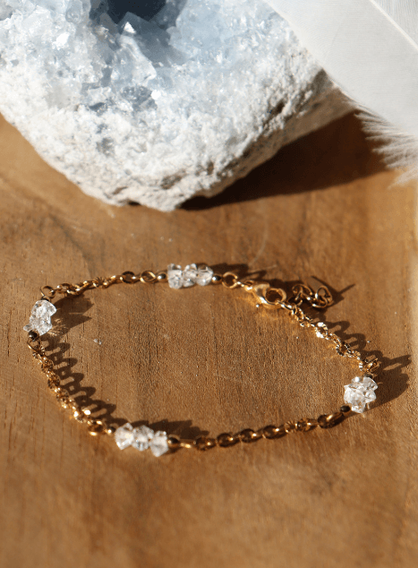 bracelet-lulu-diamant-herkimer-acier-inoxydable-dore.jpg Bracelet Lulu en acier inoxydable doré orné de cristaux de diamant d’Herkimer, bijou raffiné et lumineux présenté sur fond en bois naturel.