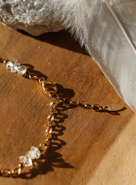 bracelet-lulu-diamant-herkimer-acier-inoxydable-dore.jpg Bracelet Lulu en acier inoxydable doré orné de cristaux de diamant d’Herkimer, bijou raffiné et lumineux présenté sur fond en bois naturel.