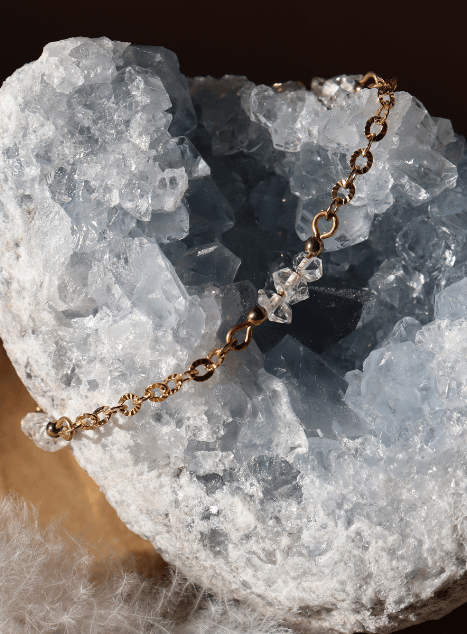 bracelet-lulu-diamant-herkimer-acier-inoxydable-dore.jpg Bracelet Lulu en acier inoxydable doré orné de cristaux de diamant d’Herkimer, bijou raffiné et lumineux présenté sur fond en bois naturel.