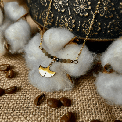Collier Sienna en acier inoxydable doré avec pendentif feuille de ginkgo et perles de jade verte, bijou délicat de 40 cm posé sur fond beige.