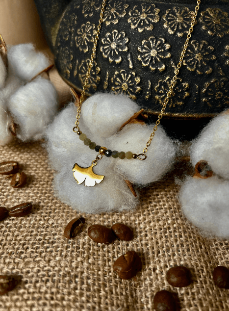 Collier Sienna en acier inoxydable doré avec pendentif feuille de ginkgo et perles de jade verte, bijou délicat de 40 cm posé sur fond beige.