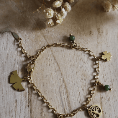 Bracelet Sissi en acier inoxydable doré orné de perles de jade verte et de charms symboliques — ginkgo, trèfle et arbre de vie — bijou porte-bonheur présenté sur fond naturel.