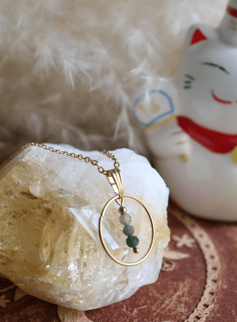 collier-sya-jade-verte-cercle-acier-inoxydable-dore-40cm.jpg Collier Sya en acier inoxydable doré avec pendentif cercle et perles de jade verte, bijou raffiné de 40 cm posé sur fond beige doux.