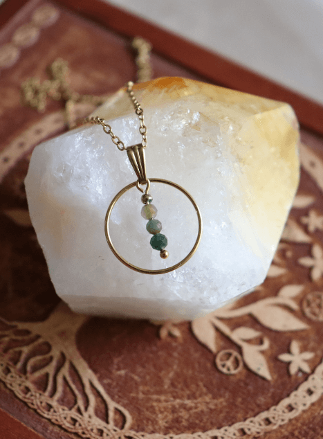 collier-sya-jade-verte-cercle-acier-inoxydable-dore-40cm.jpg Collier Sya en acier inoxydable doré avec pendentif cercle et perles de jade verte, bijou raffiné de 40 cm posé sur fond beige doux.