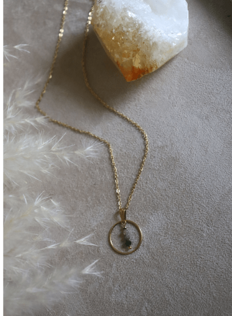 collier-sya-jade-verte-cercle-acier-inoxydable-dore-40cm.jpg Collier Sya en acier inoxydable doré avec pendentif cercle et perles de jade verte, bijou raffiné de 40 cm posé sur fond beige doux.