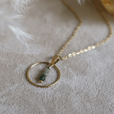 Collier Sya en acier inoxydable doré avec pendentif cercle et perles de jade verte, bijou raffiné de 40 cm posé sur fond beige doux.